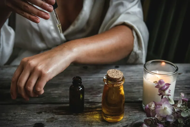 Hands preparing aromatherapy oils beside candles and dried flowers