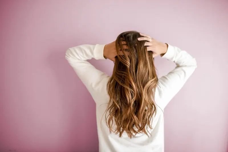 Woman with long wavy hair seen from behind against a pink wall