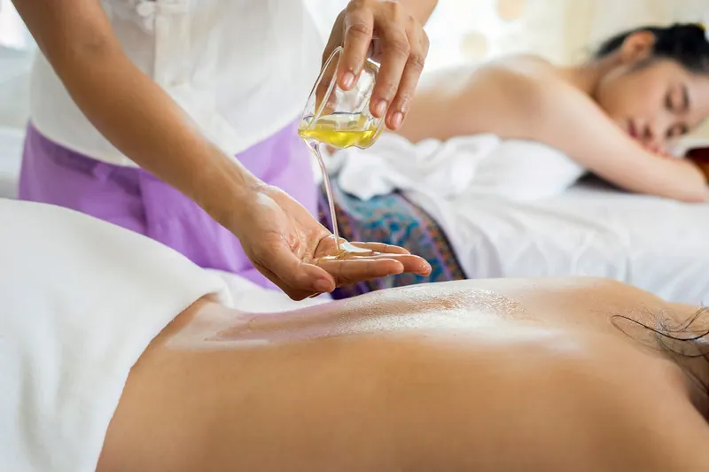 Therapist pouring massage oil for a client on a spa bed