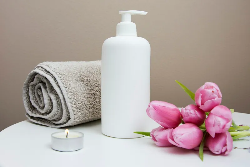 Rolled towel, lotion bottle, candle and pink tulips in a spa