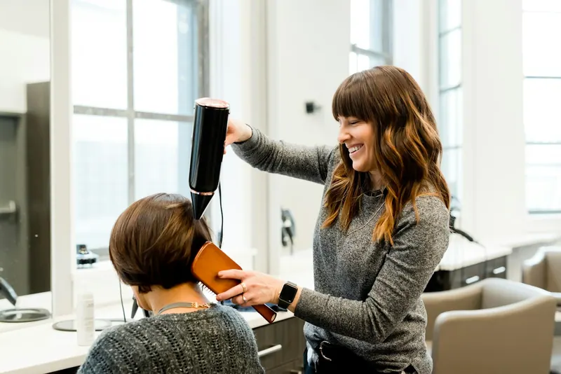 Stylist blow-drying a client's short hair in a bright salon