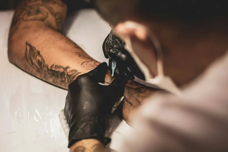 Tattoo artist in black gloves tattooing a client